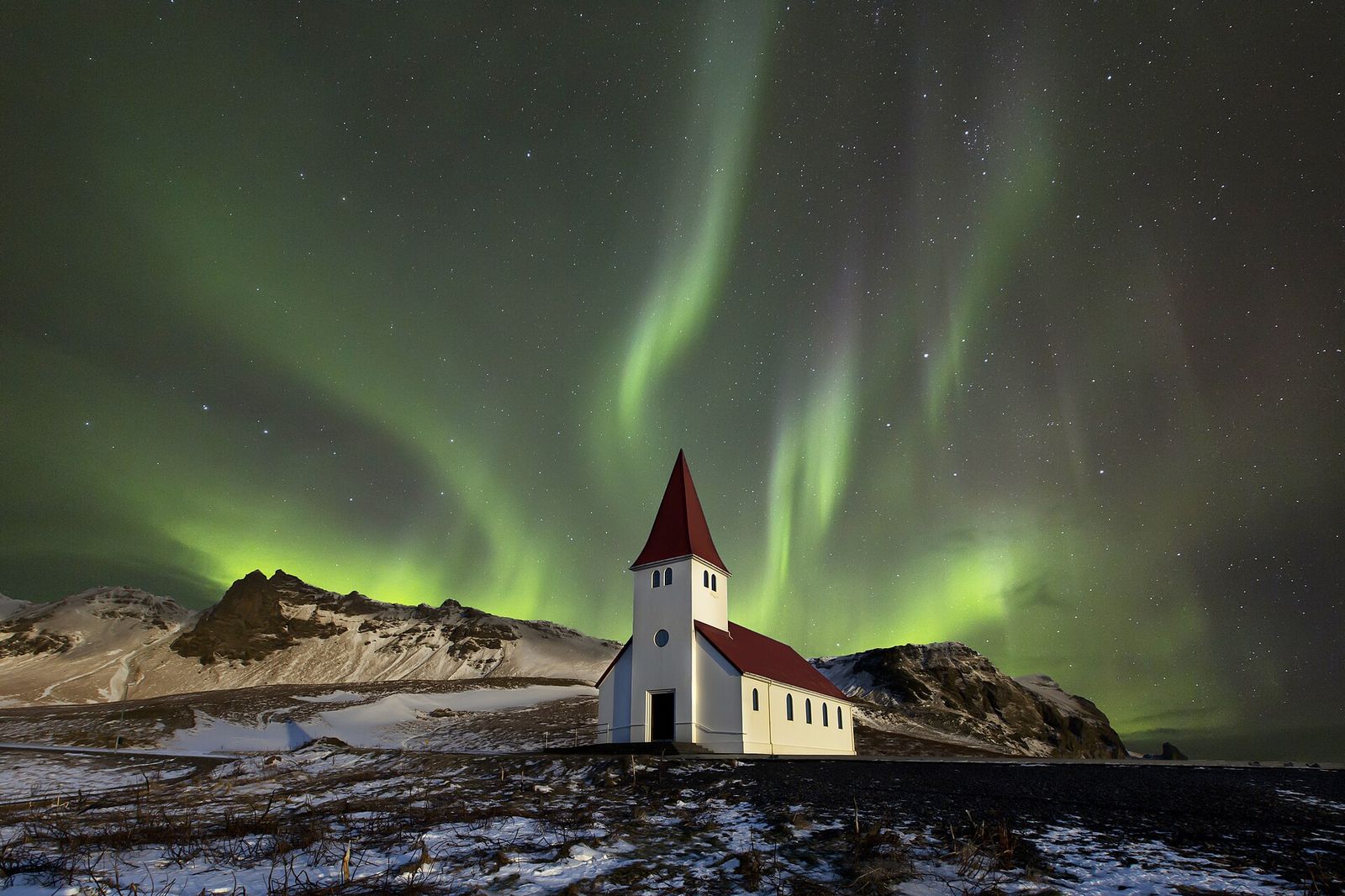 Aurora boreal sobre uma igreja isolada na Islândia
